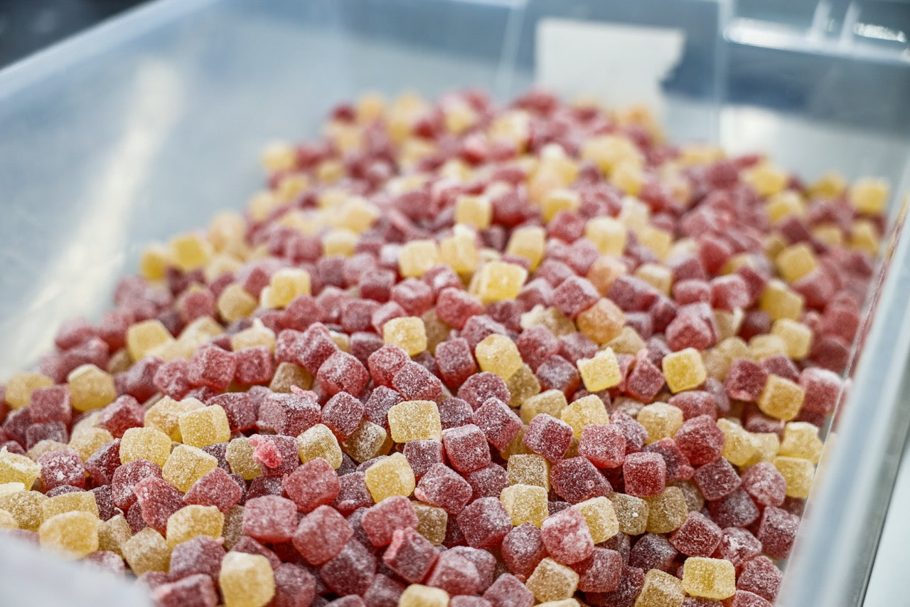 Close-up of Pure Shenandoah Rest CBD Gummies in bulk, showing sugar-coated red and yellow cubes in a production bin during manufacturing.